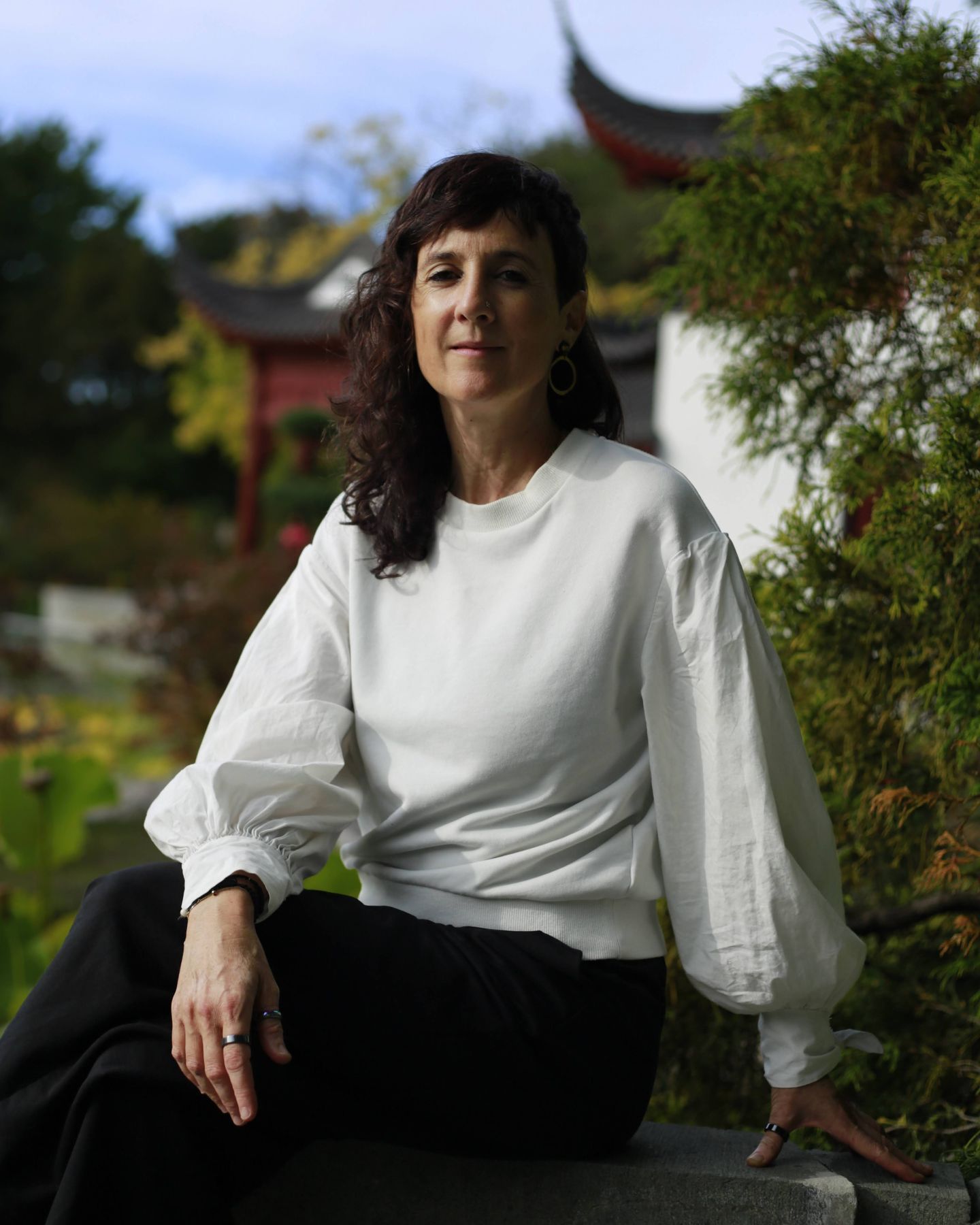 Julie Gazard, dressed in white, sitting on a low stone wall in front of a pavilion at the Chinese Garden.