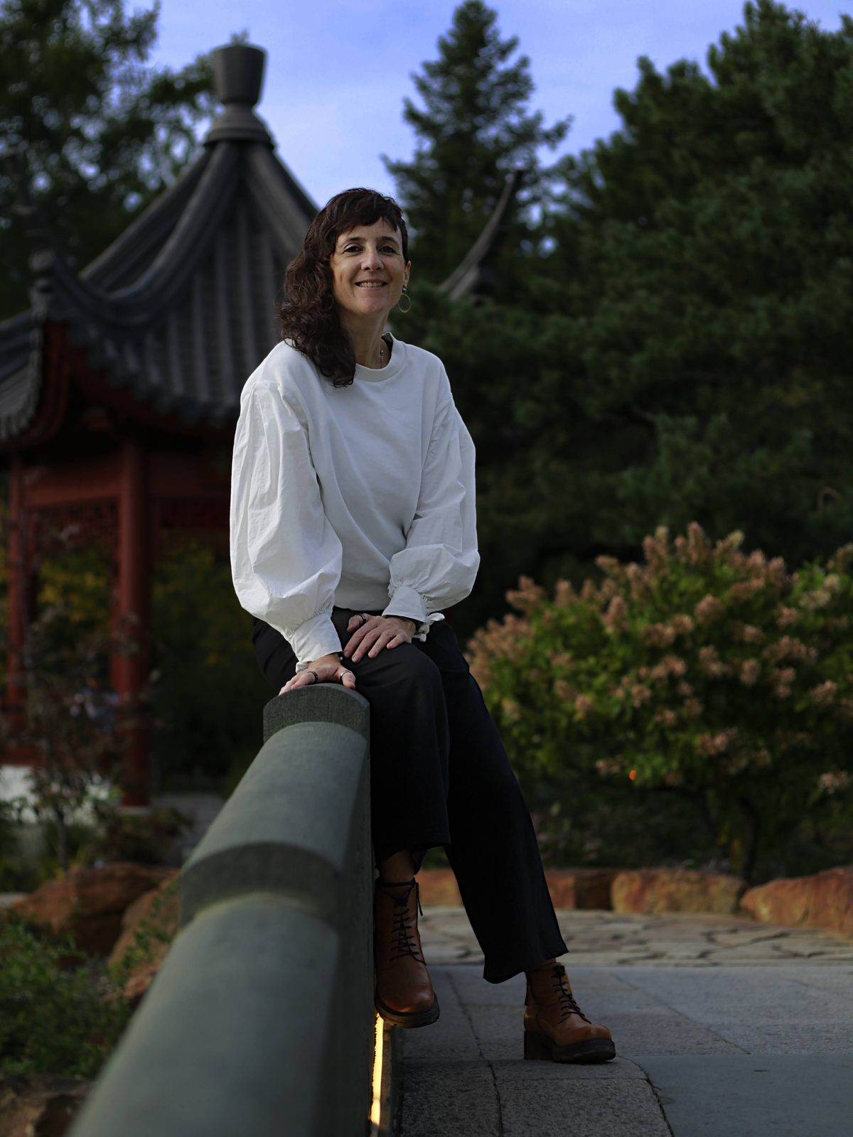 Julie Gazard, souriante, en blouse blanche, assise sur un muret devant un pavillon du Jardin de Chine.