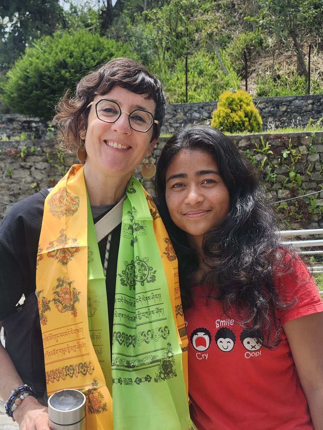 Julie Gazard, smiling, a yellow and a green welcome scarf around her neck, her head against that of a young Nepali woman in a red T-shirt.