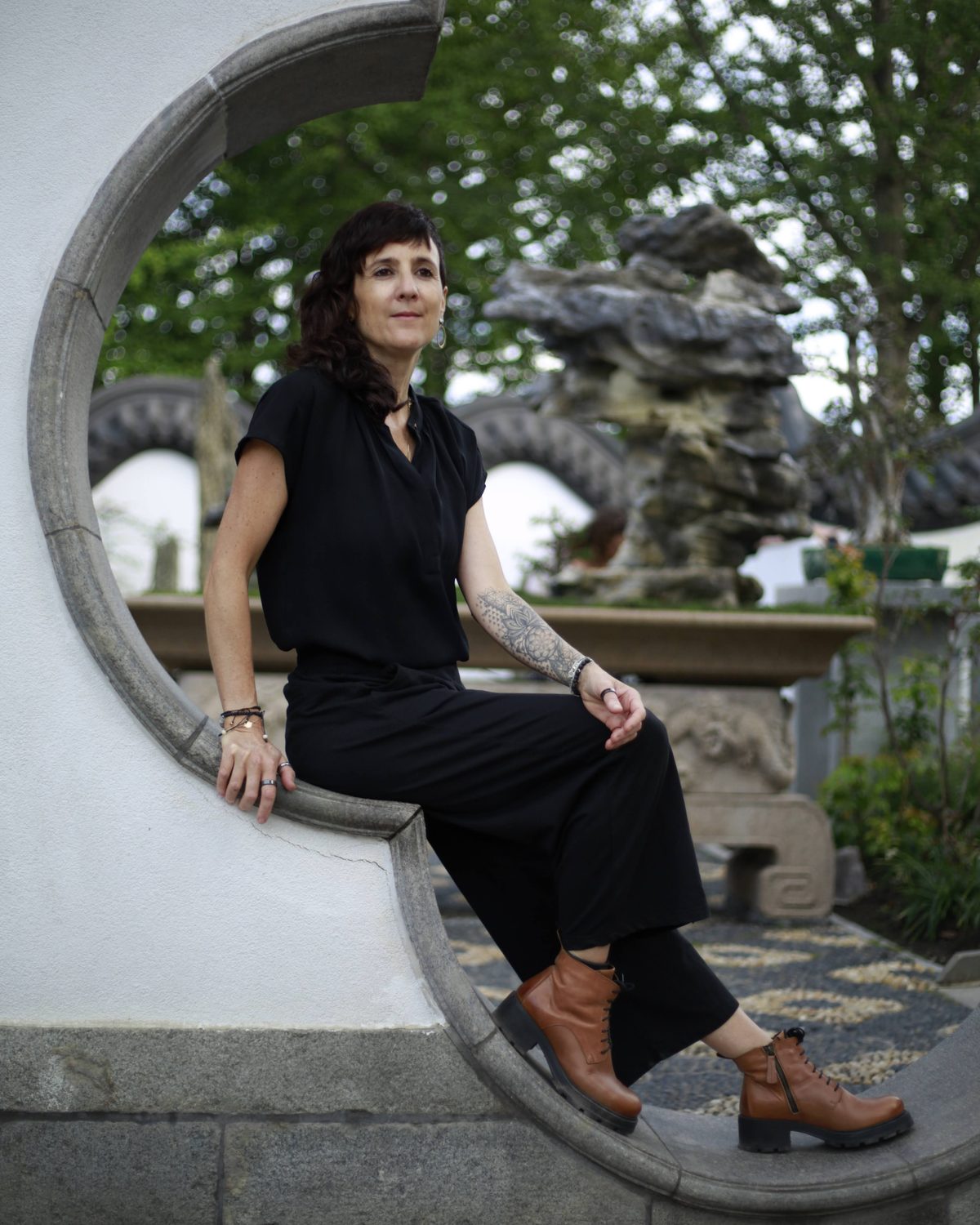 Julie Gazard, dressed in black, sitting in the round opening of a white wall, at the Chinese Garden.