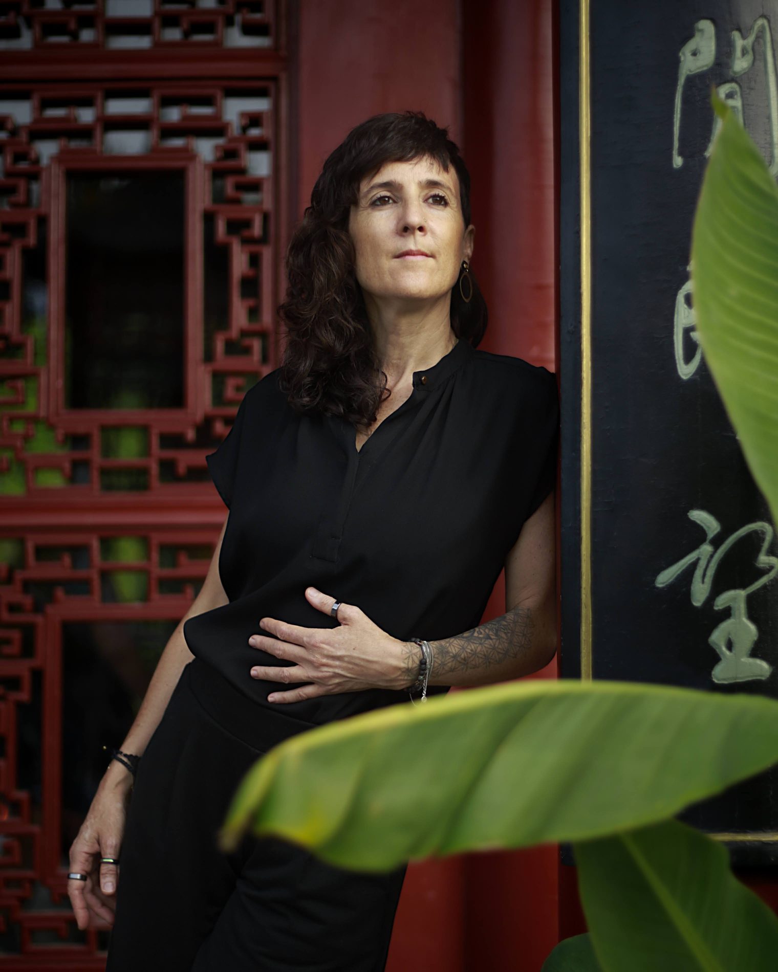 Julie Gazard, in a black shirt, in front of panels of Chinese calligraphy and a banana leaf.