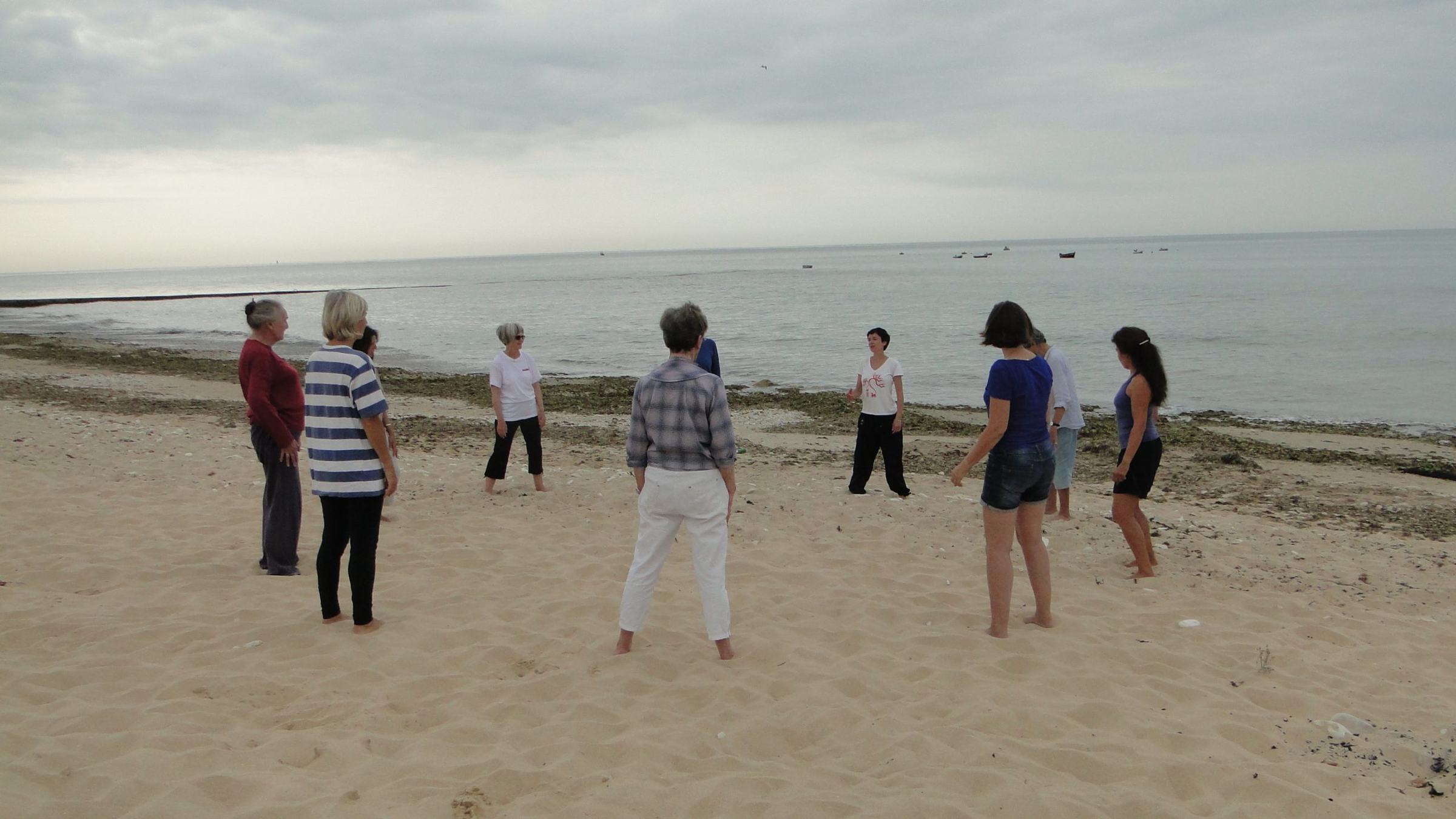 Julie Gazard leads a qi gong circle on a beach on Île de Ré, facing the sea.