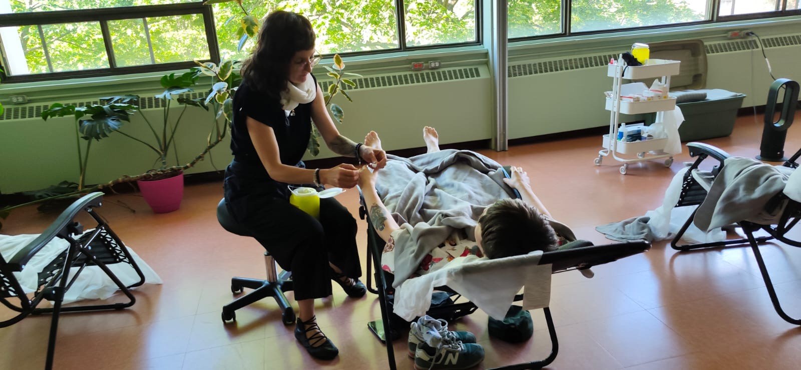 Julie Gazard pose une aiguille sur la main d'une personne allongée dans une chaise inclinable, au SLAB.
